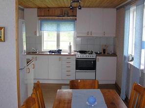 A compact kitchen with white cabinets, a stove, and a dining table with chairs. - 6 Person Holiday Home in Hacksvik (Håcksvik)