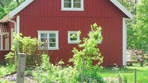 Ein rotes Bauernhaus mit zwei Fenstern und weißem Zierstreifen.