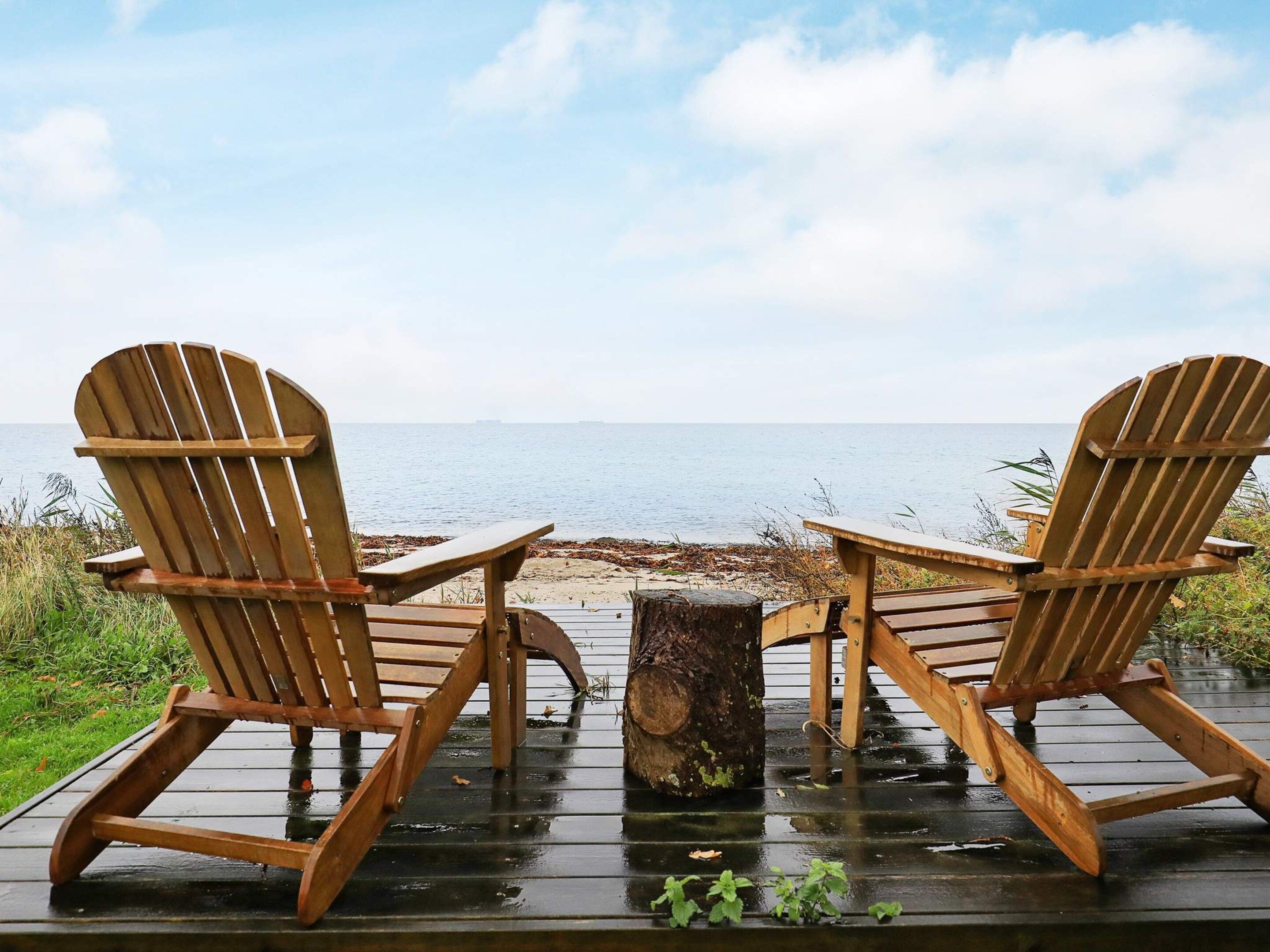 Two wooden Adirondack chairs facing a body of water with a wooden deck in the foreground.