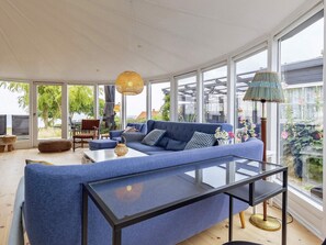 Een moderne woonkamer met een blauwe bank, een glazen salontafel en grote ramen met uitzicht op het landschap.
