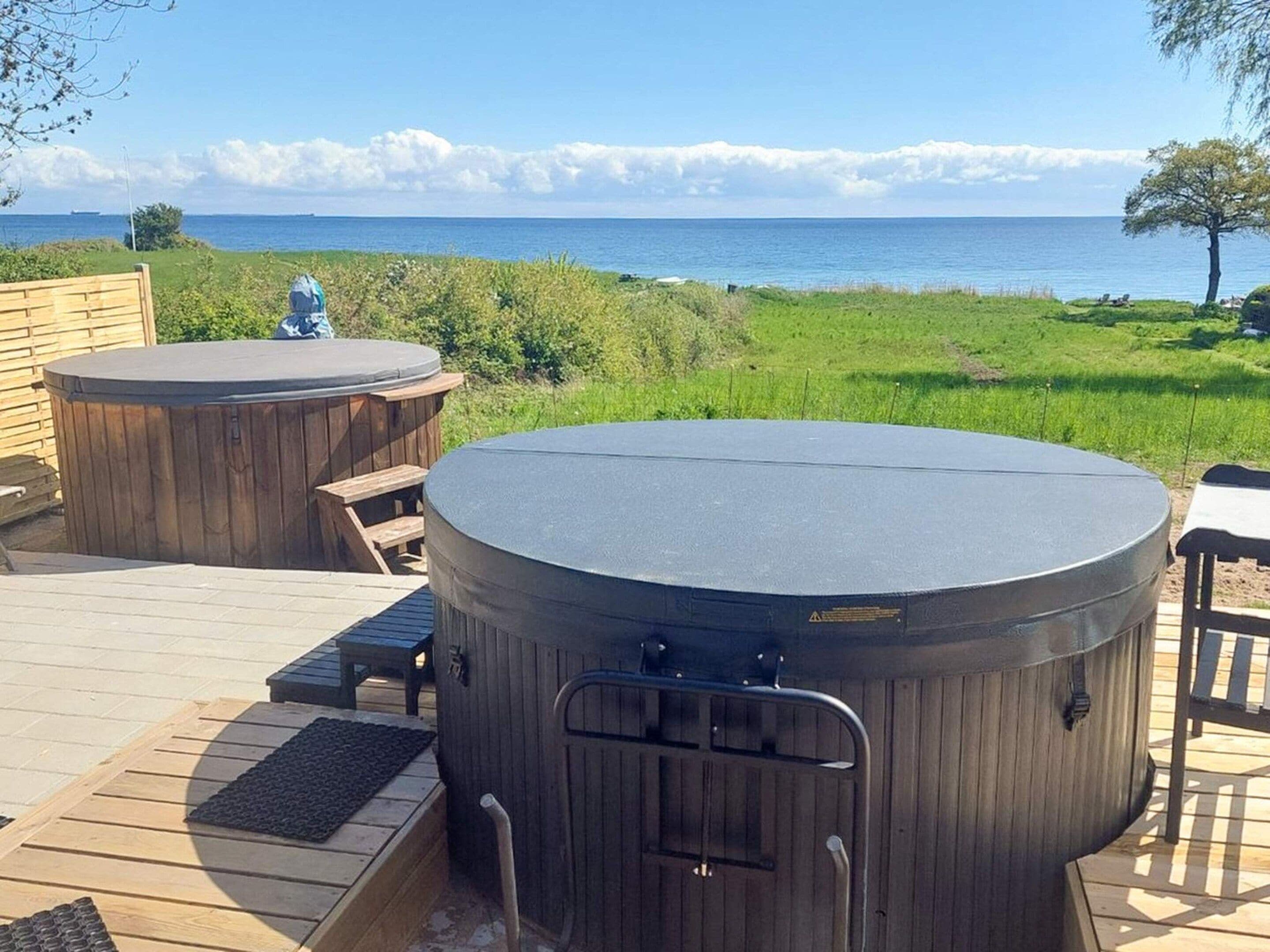 A hot tub area with a view of the sea, wooden deck, and seating.