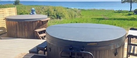 A hot tub area with a view of the sea, wooden deck, and seating.