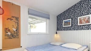 Una camera da letto con un letto, una finestra con persiane, una parete con carta da parati decorata e un'opera d'arte appesa.