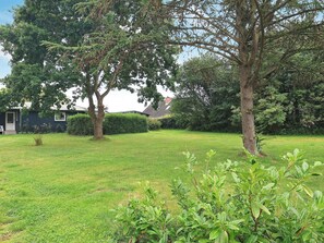 A residential property with a well-maintained lawn, mature trees, and a small house with a visible front door and windows. - 8 Person Holiday Home in Tranekaer (Tranekaer)