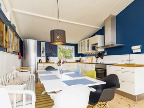 A modern kitchen with white cabinets, a central island, and a dining area with a white table and chairs. - 8 Person Holiday Home in Tranekaer (Tranekaer)