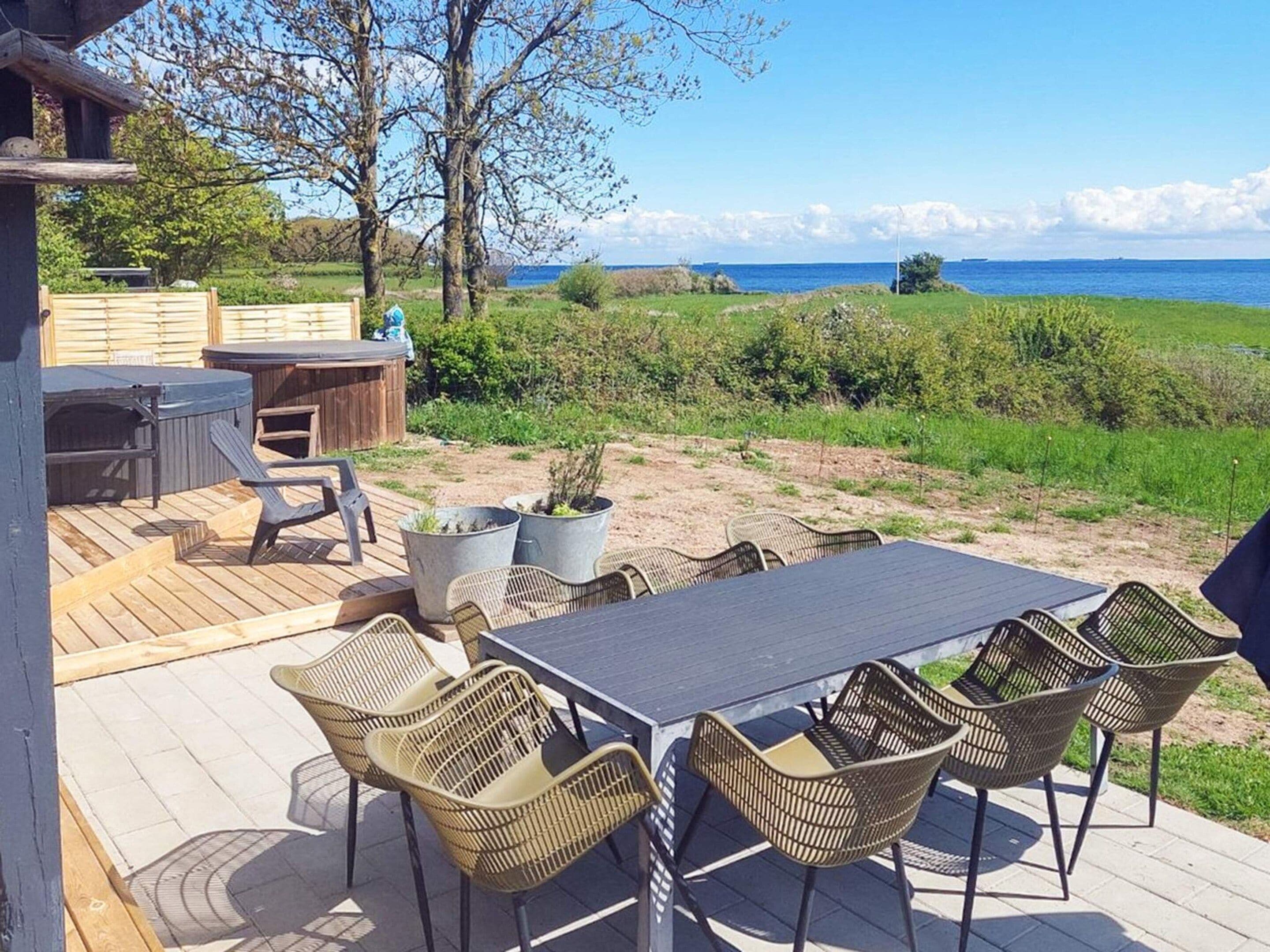 A deck with outdoor furniture, a hot tub, and a view of the sea.