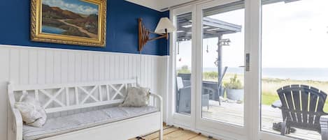 A room with a white bench, a framed painting, and a view through a glass door to an outdoor deck.