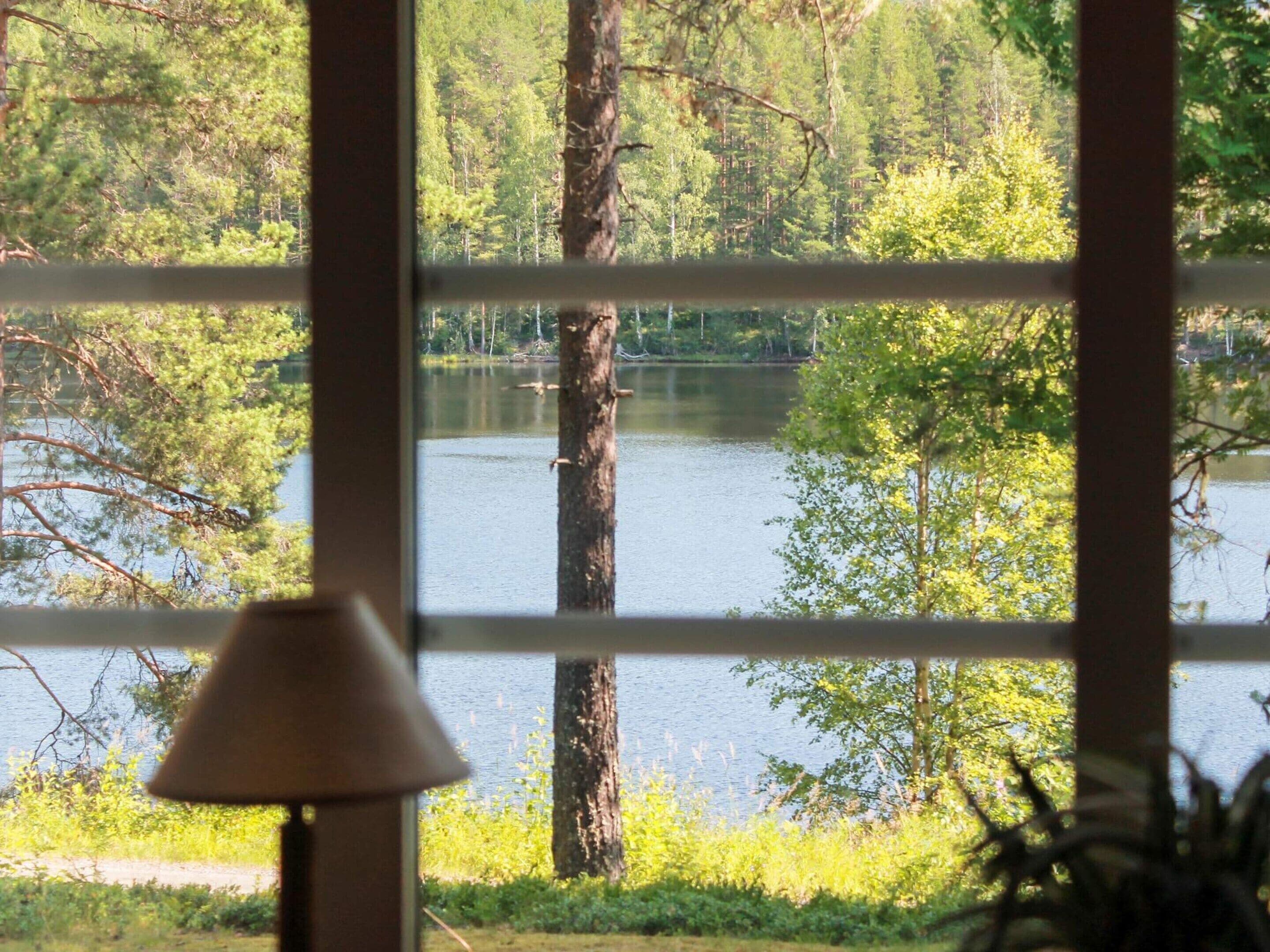 A view through a window with a lamp, showcasing a lake surrounded by trees.