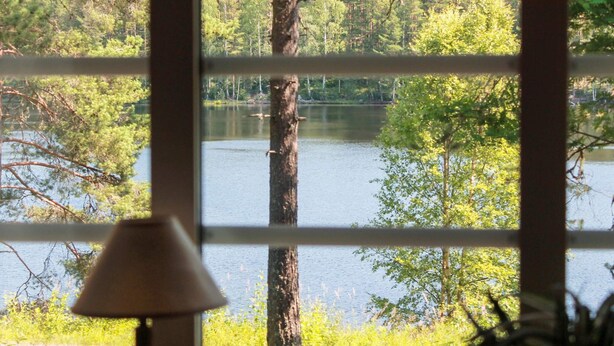 A view through a window with a lamp, showcasing a lake surrounded by trees. - 4 Person Holiday Home in Torsby (Torsby)