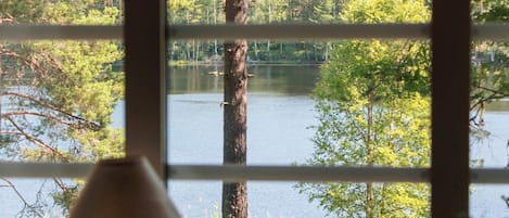 A view through a window with a lamp, showcasing a lake surrounded by trees.
