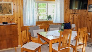 Ein Zimmer mit Holzwänden, einem Esstisch, Stühlen, einem Fernseher und einem Fenster mit Vorhängen.