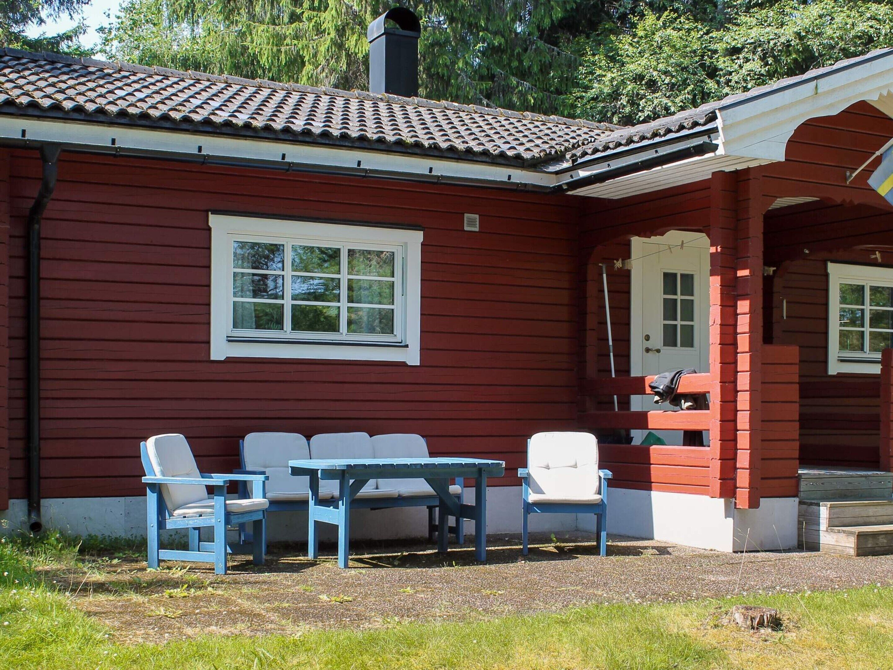 Une maison en bois rouge avec un toit en tuiles, une fenêtre blanche et une véranda avec des chaises bleues et une table.
