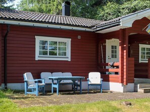 A red wooden house with a tiled roof, a white window, and a porch with blue chairs and a table. - 4 Person Holiday Home in Torsby (Torsby)