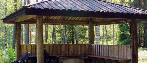 A wooden gazebo with a sloped roof, a bench, and a concrete planter.
