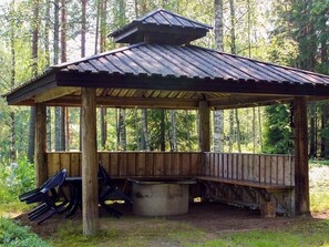 A wooden gazebo with a sloped roof, a bench, and a concrete table. - 4 Person Holiday Home in Torsby (Torsby)