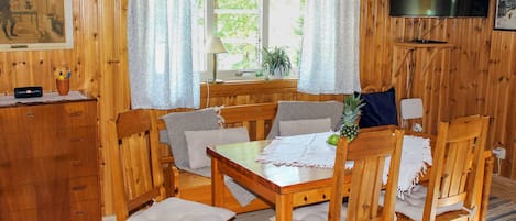 A wooden room with a dining table, chairs, a television, and a window with curtains.