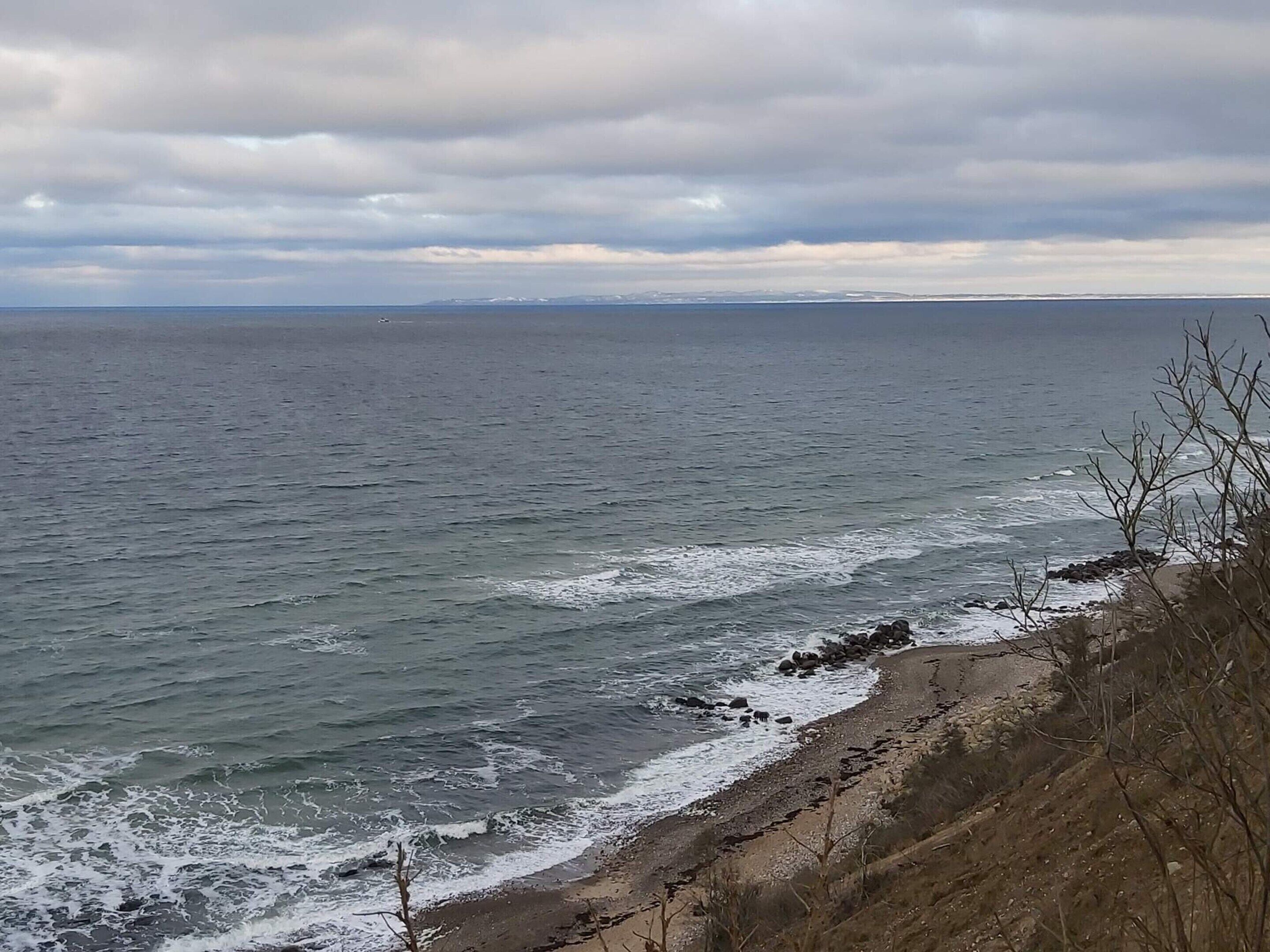 Un paysage côtier avec une rive rocheuse, des vagues et un ciel nuageux.