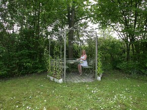 A woman sitting on a bench under a metal gazebo in a garden. - 4 Star Holiday Home in Dronningmolle (Dronningmolle)
