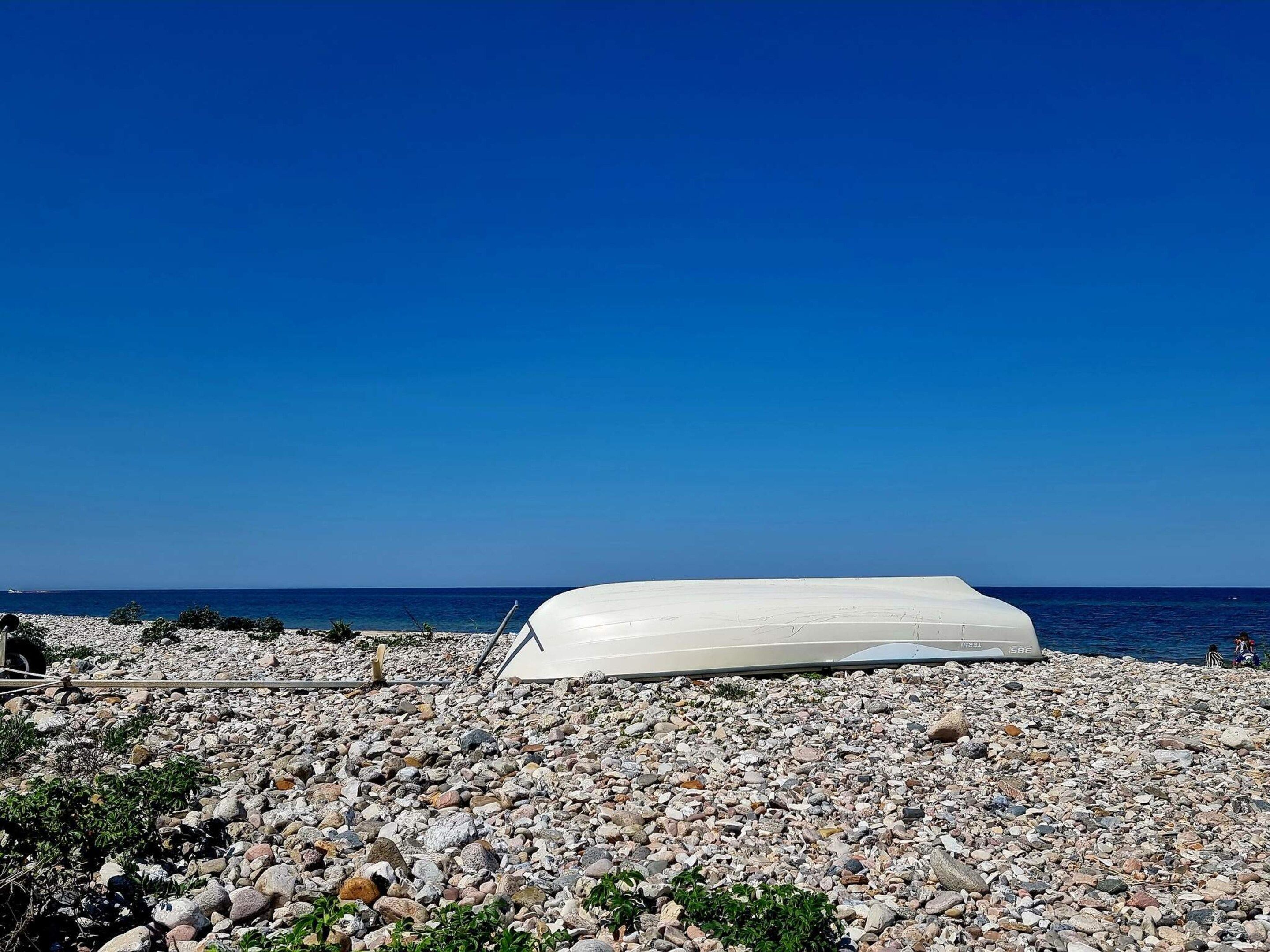A white boat on a rocky beach with a clear blue sky.