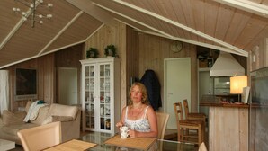 Een gezellige kamer met een houten plafond, een witte kast met glazen deuren, een eettafel met stoelen en een keukenhoek met een fornuis en een lamp.