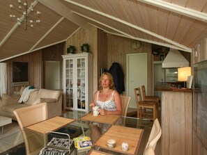 A cozy room with a wooden ceiling, a white cabinet with glass doors, a dining table with chairs, and a kitchen area with a stove and a lamp. - 4 Star Holiday Home in Dronningmolle (Dronningmolle)
