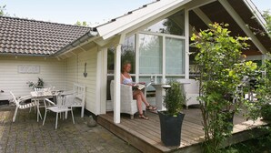 Een overdekte buitenruimte met een tafel, stoelen, een potplant en een persoon die een boek leest.