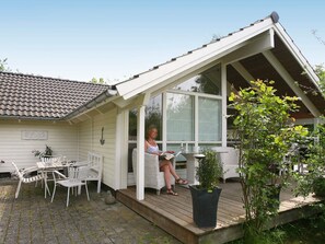 A covered outdoor seating area with a table and chairs, a potted plant, and a person reading a book. - 4 Star Holiday Home in Dronningmolle (Dronningmolle)