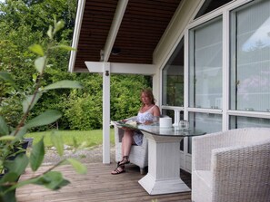 A covered outdoor seating area with a table and chairs, surrounded by greenery. - 4 Star Holiday Home in Dronningmolle (Dronningmolle)