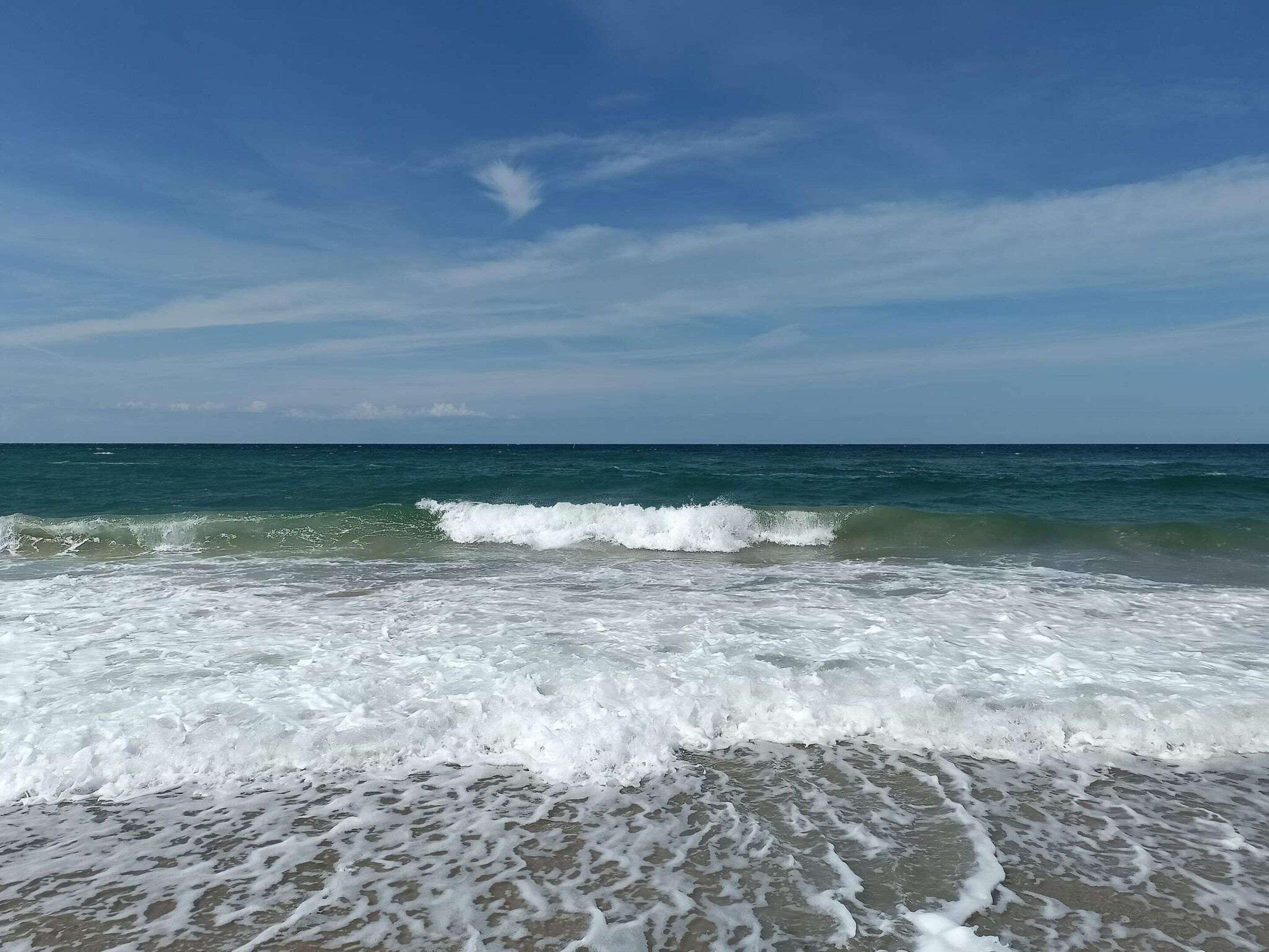 A beach with waves, clear sky, and distant horizon.
