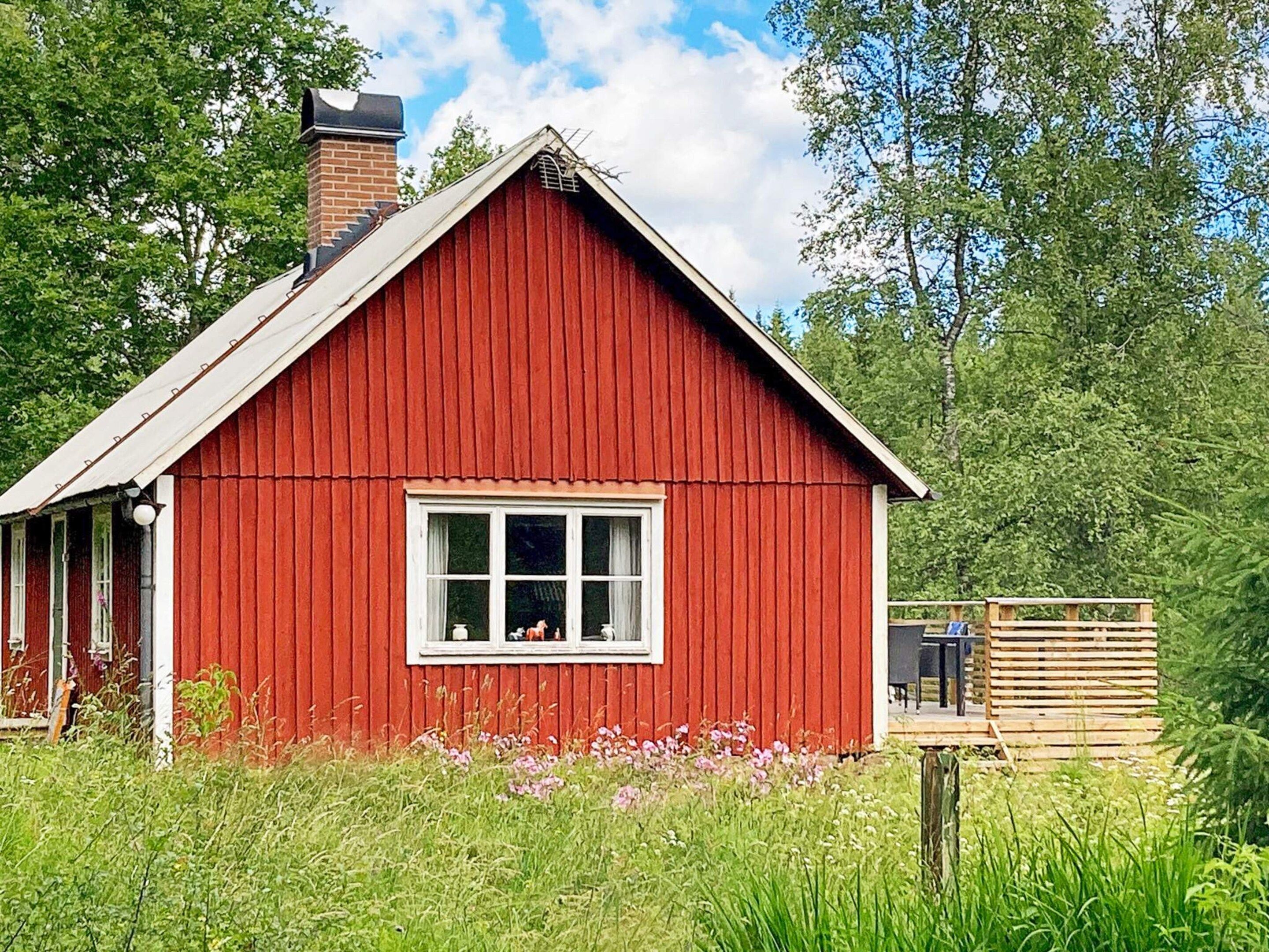 A red wooden building with a gabled roof, a window, and a small porch area.