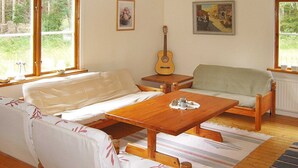Un salon chaleureux avec un canapé, une table basse en bois et une guitare. De grandes fenêtres offrent une vue sur la verdure environnante.