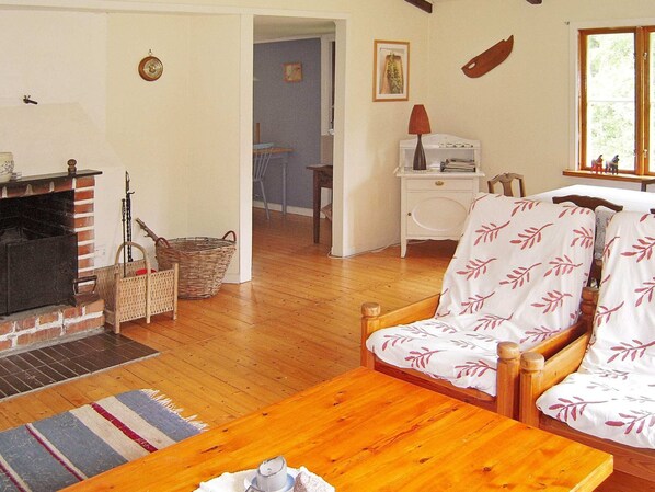 A cozy living room with a fireplace, wooden furniture, and a view of the outside through a window. - 6 Person Holiday Home in Osby (Osby)