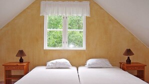 Ein Zimmer mit zwei Einzelbetten, einem Fenster mit weißem Vorhang und zwei Nachttischen mit Lampen.