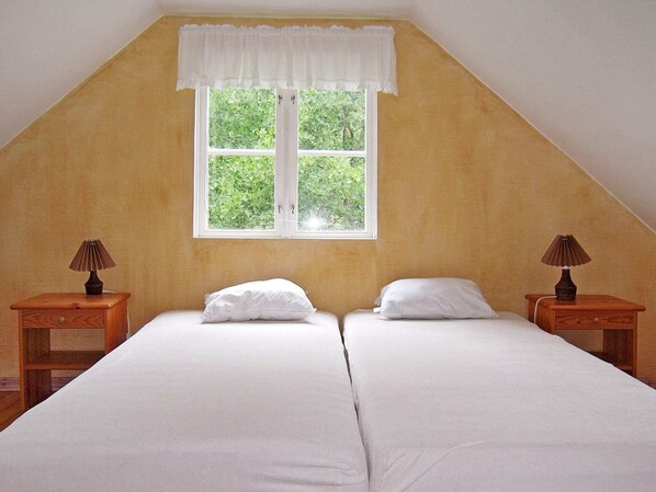 A room with two single beds, a window with a white valance, and two bedside tables with lamps.