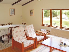 A cozy room with a dining table, two chairs, a sofa, and a window with a view of greenery.