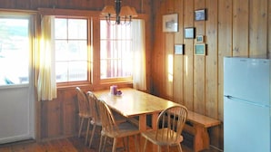Una habitación con paneles de madera, una mesa de madera, cuatro sillas, un banco, una araña y un refrigerador.