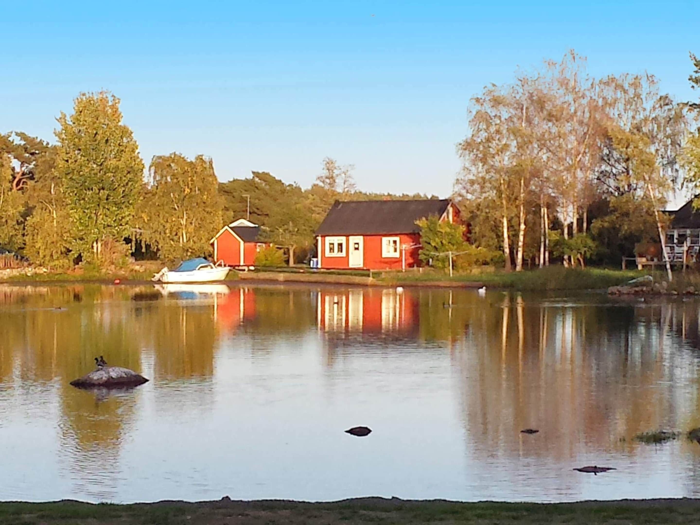 A calm lake with a red house and a boat on the shore.