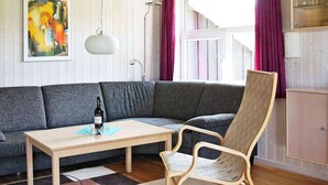 Ein modernes Wohnzimmer mit einem grauen Ecksofa, einem Holztisch, einem gewebten Sessel und einem gemusterten Teppich.