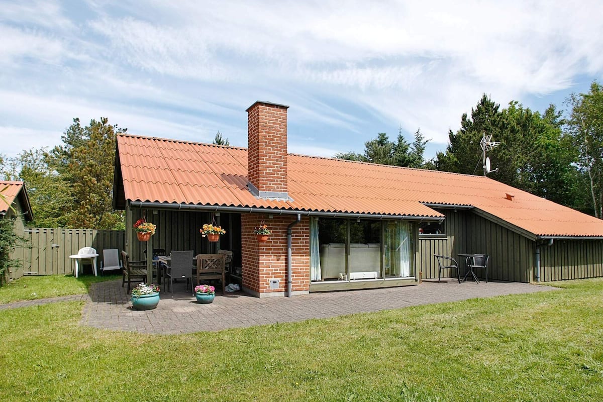 A brick house with a red roof, a chimney, and a covered patio area with outdoor furniture.