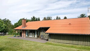 A two-story building with a red-tiled roof, a brick chimney, and a covered patio area with outdoor furniture. - 8 Person Holiday Home in Fjerritslev-by Traum (Fjerritslev)