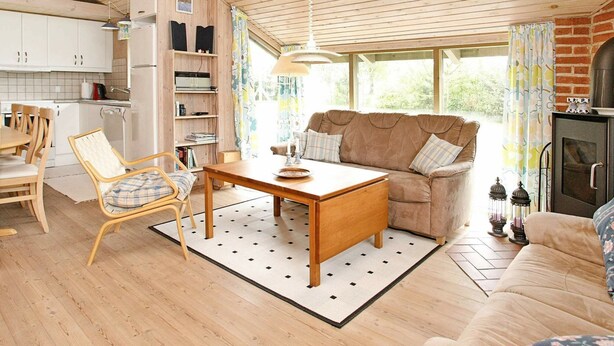 A cozy living room with a sofa, a wooden dining table, and a kitchen area with cabinets and a stove. - 8 Person Holiday Home in Fjerritslev-by Traum (Fjerritslev)