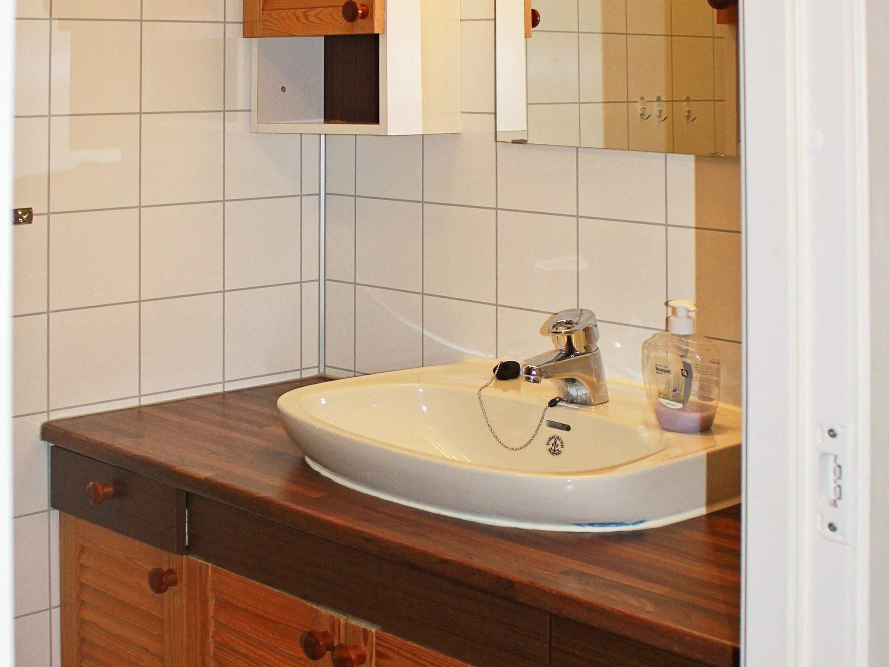 A bathroom with a white sink, wooden cabinets, a mirror, and a towel rack.