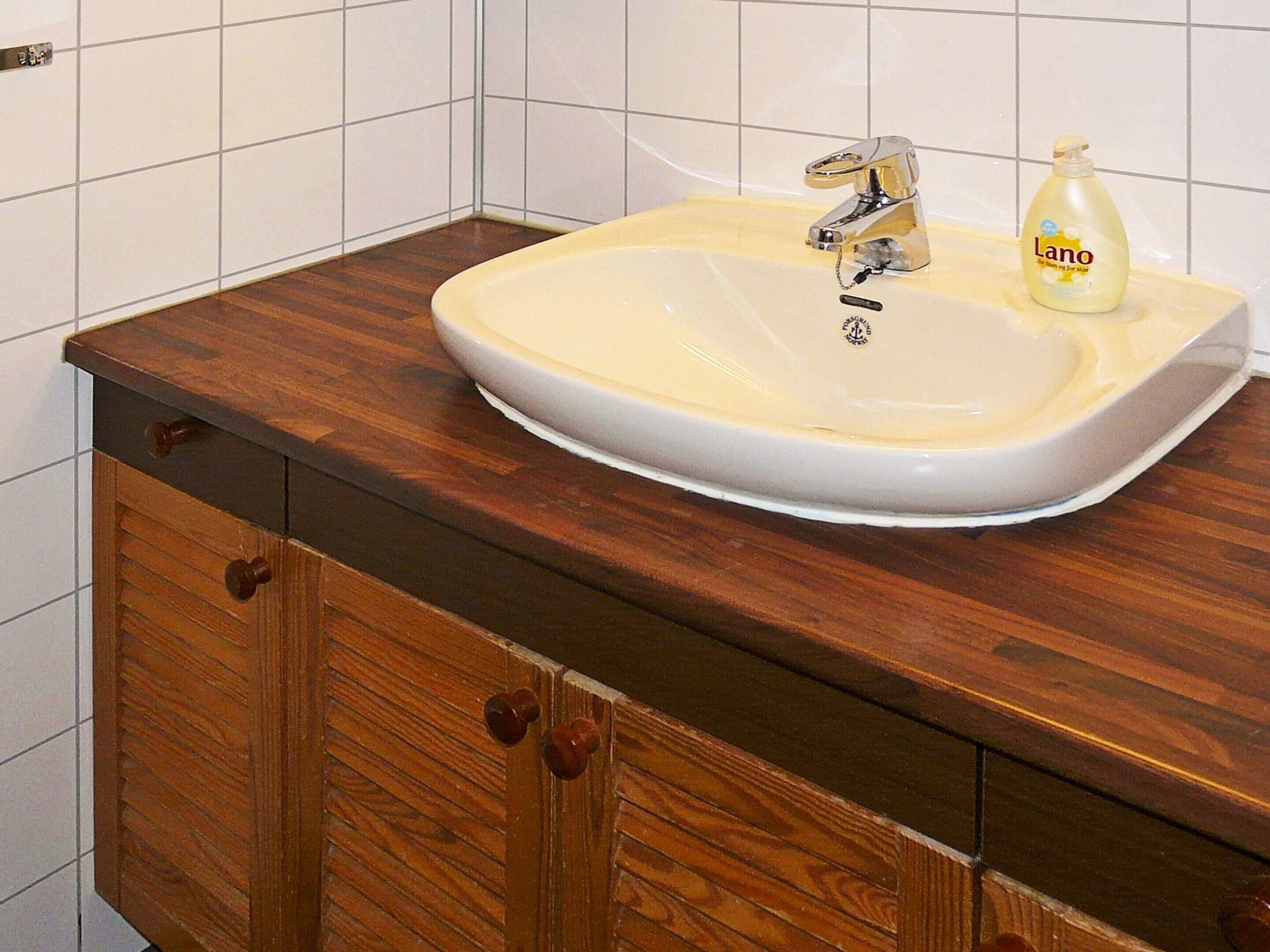Une salle de bain avec un meuble-lavabo en bois, un lavabo blanc et une bouteille de savon Lano.