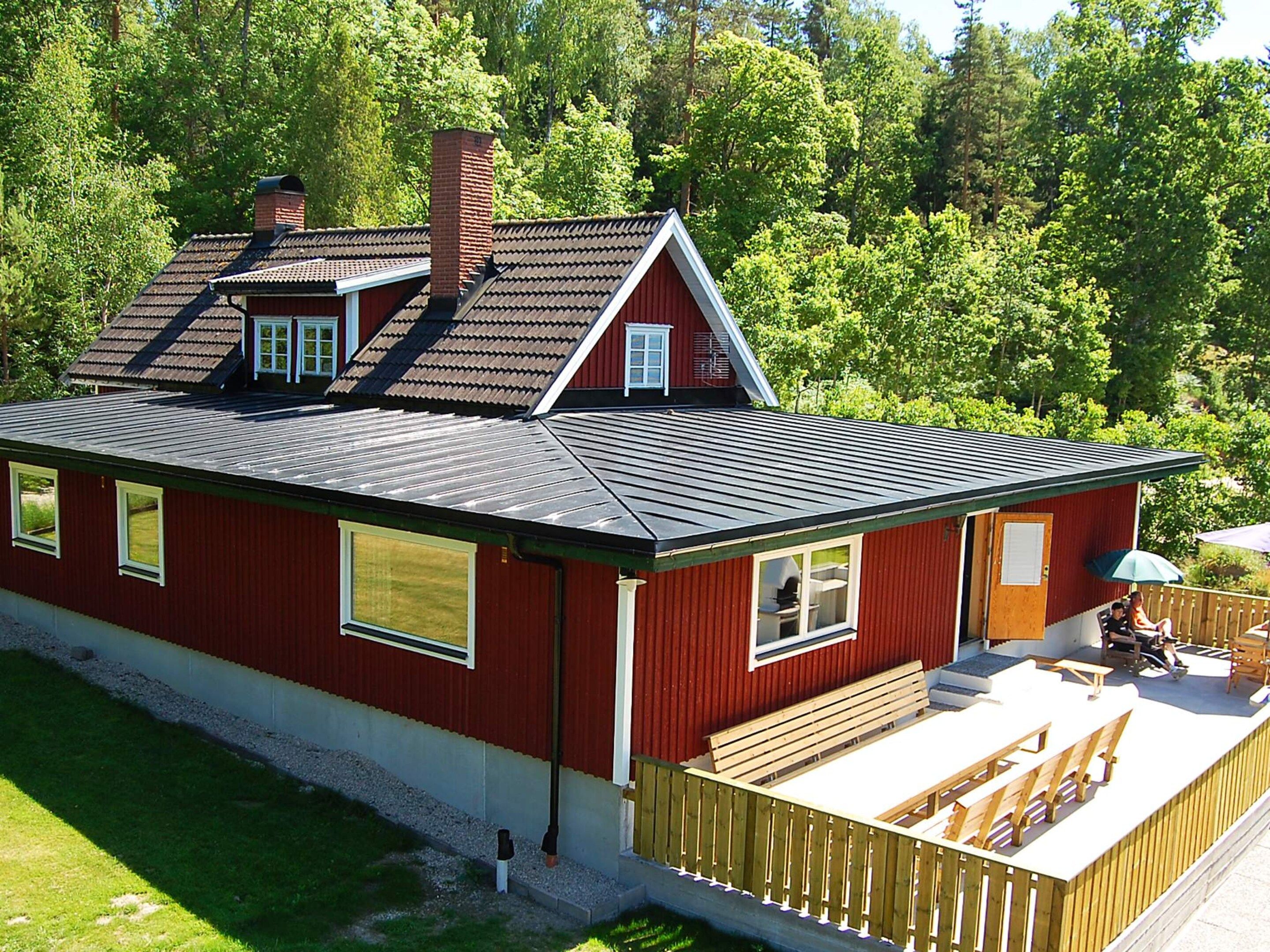 A red house with a sloped roof, a chimney, and a deck with wooden furniture.
