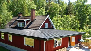 A red house with a sloped roof, a chimney, and a deck with wooden furniture.