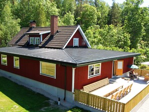 A red house with a sloped roof, a chimney, and a deck with wooden furniture.