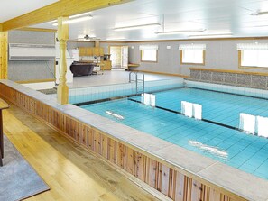 Une piscine avec une terrasse en bois, un ventilateur de plafond et un coin cuisine à l’arrière-plan.