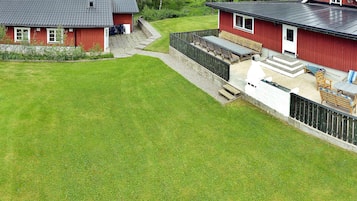 A red building with a sloped roof, a covered patio area with outdoor furniture, and a well-maintained lawn.