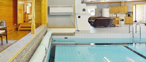 Piscina com deck revestido em azulejo, paredes de madeira e área de cozinha com armários e eletrodomésticos.