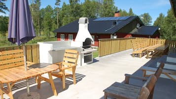 An outdoor patio area with wooden furniture, a barbecue grill, and a house in the background.